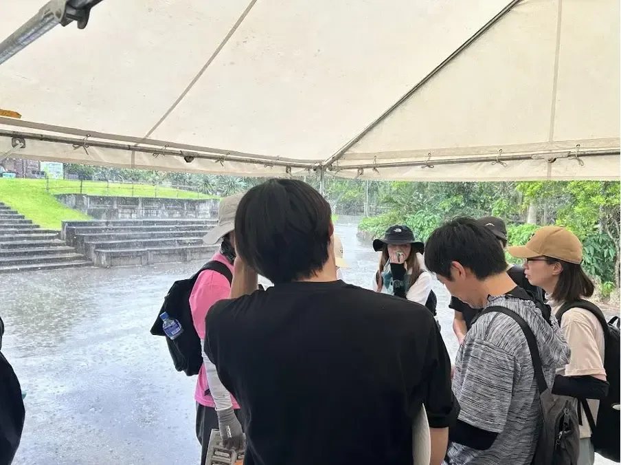 テントの下で雨をしのぎながらクエストを続ける参加者