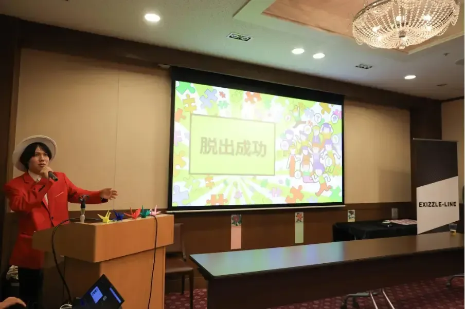 スクリーンに「脱出成功」と表示された会場とMC